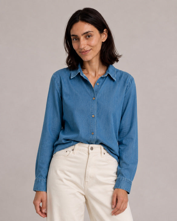 Blue relaxed denim shirt, alternate front view with a small front tuck into ivory jeans.