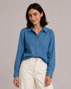 Blue relaxed denim shirt, alternate front view with a small front tuck into ivory jeans.