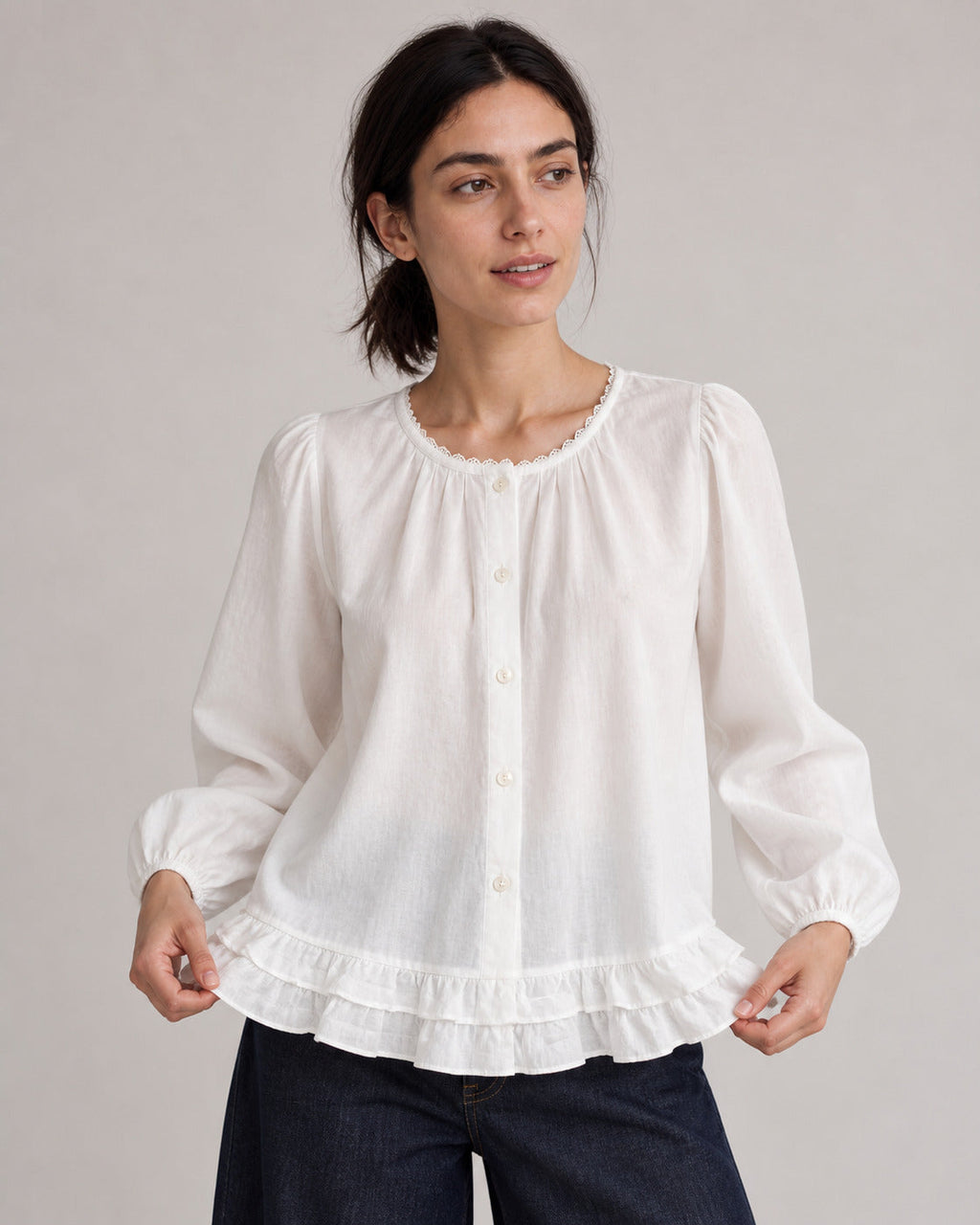 White puff-sleeve blouse on a model gently holding the ruffled hem.