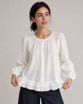 White puff-sleeve blouse on a model gently holding the ruffled hem.