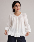 White puff-sleeve blouse on a model gently holding the ruffled hem.