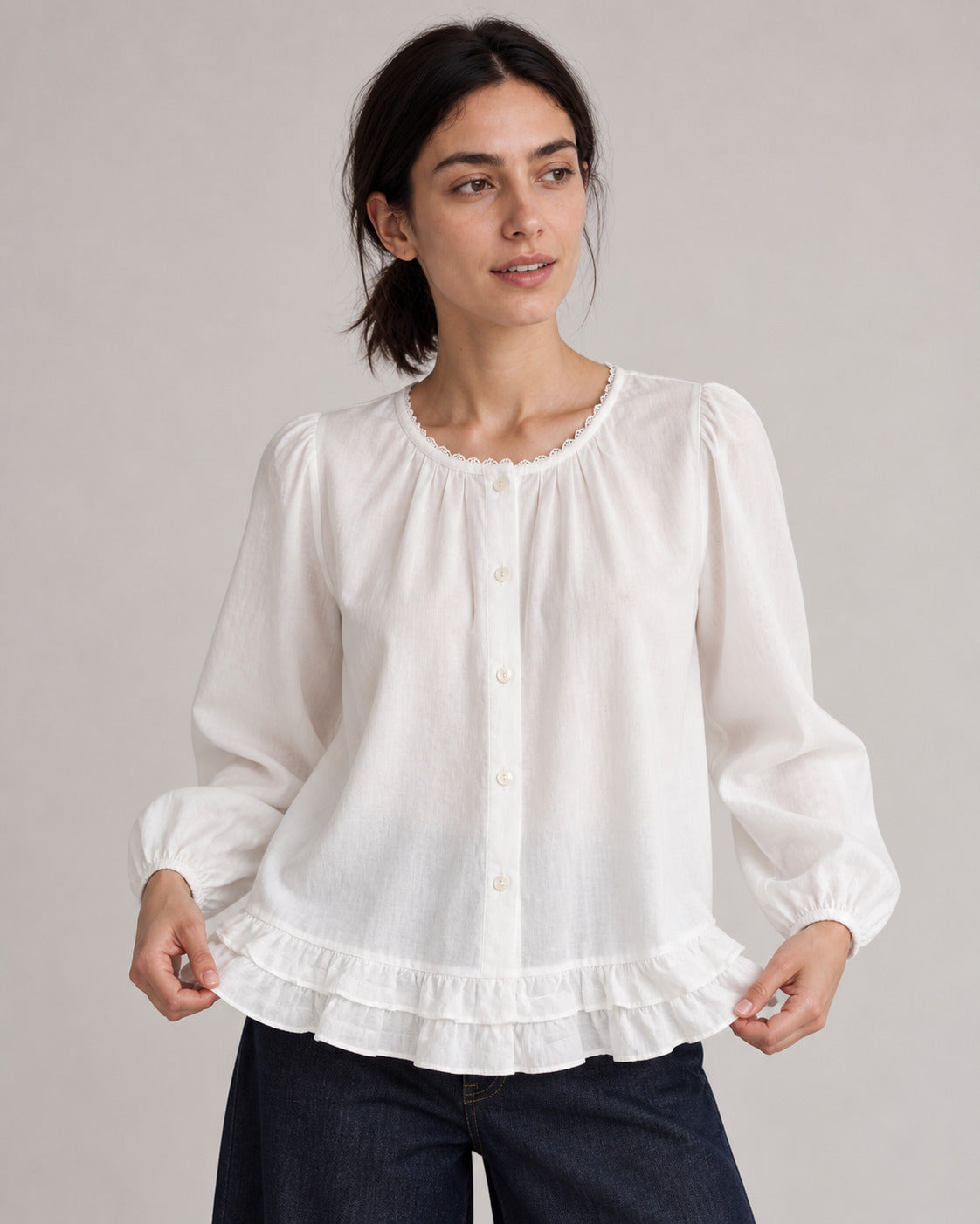 White puff-sleeve blouse on a model gently holding the ruffled hem.