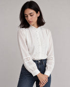White lace-trim stand-collar blouse tucked into dark jeans, with hands resting below the waist.