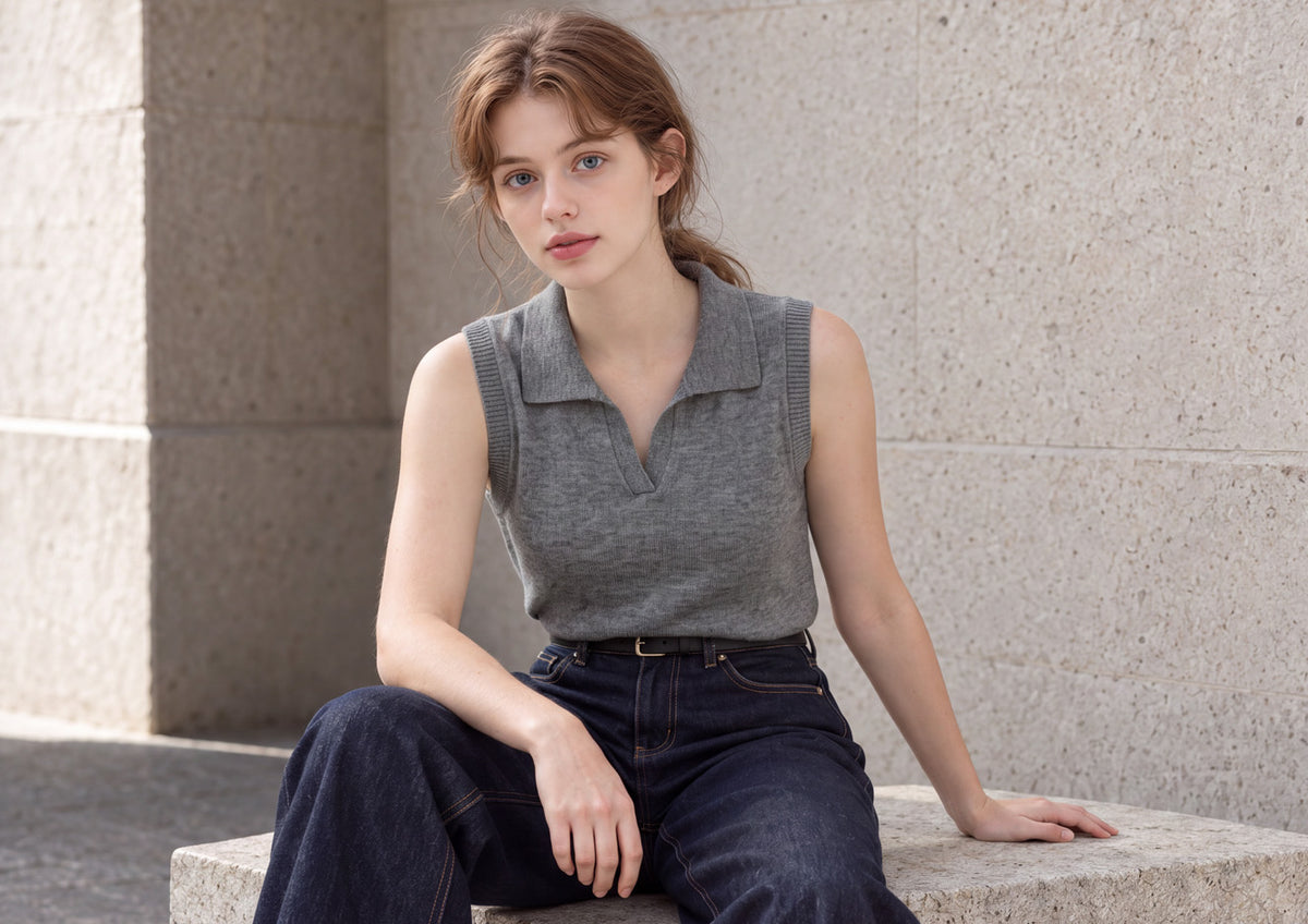 Gray sleeveless knit and raw-indigo jeans, seated on a stone bench